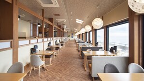 A modern dining area with wooden tables and chairs, large windows, and a herringbone floor pattern. - Sanuki mansion (Kanonji)