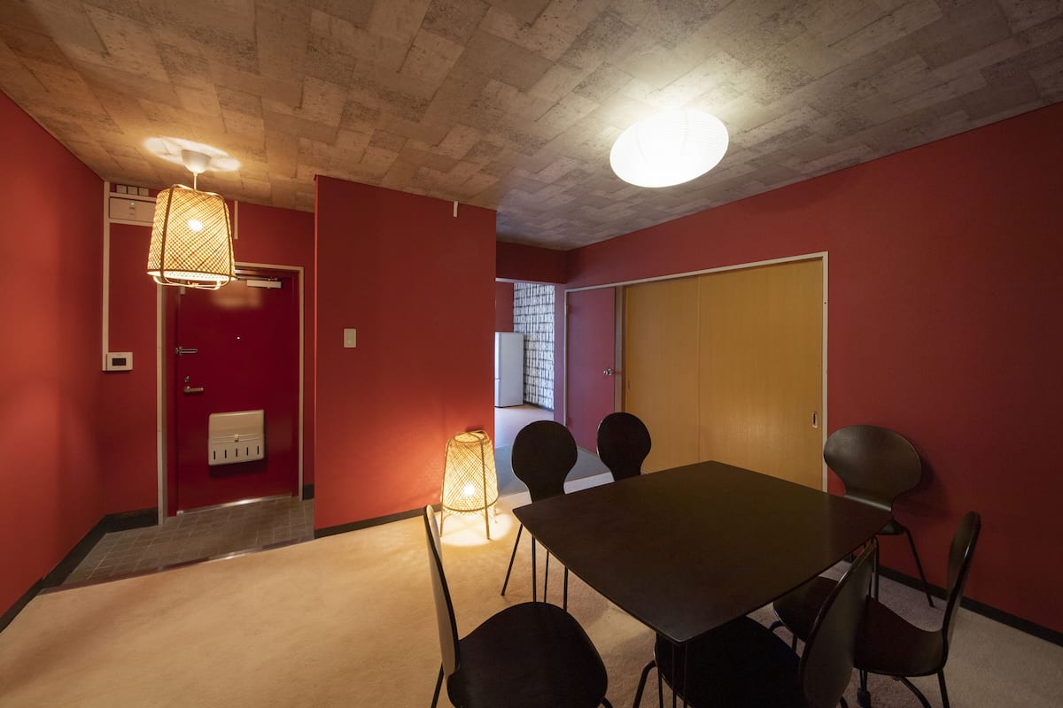 A conference room with a table and chairs, a red wall, a ceiling with a textured pattern, and a door with a handle.
