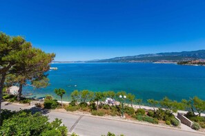 Una carretera costera con vistas despejadas al mar, algunos árboles y un pueblo lejano.
