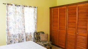 A bedroom with a bed, a chair, a wooden wardrobe, and a floral curtain. - Cozy Single Apartment (Castries)