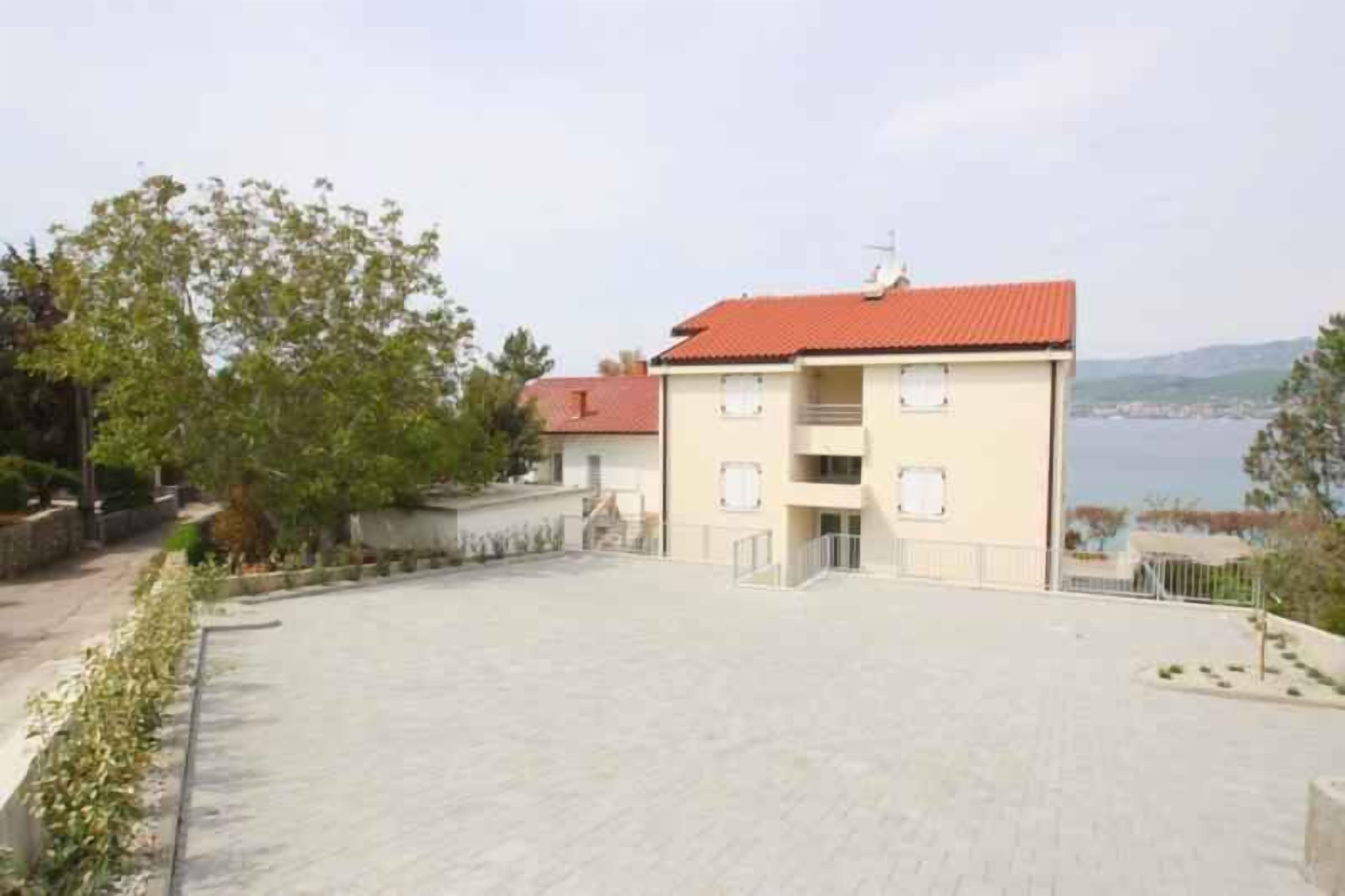 A two-story building with a red roof, a paved courtyard, and a view of the sea.