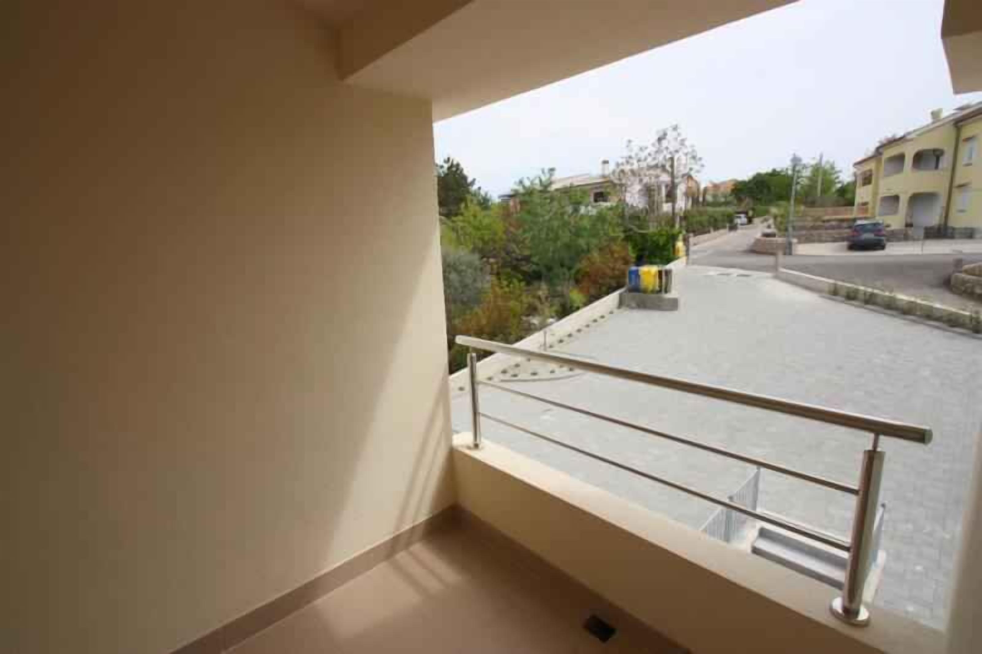 A balcony with a metal railing overlooking a street with buildings and parked cars.