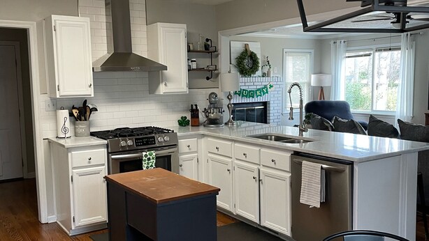 A modern kitchen with white cabinets, a central island, and a dining area with a round table. - Masters Rental Conveniently Located to Augusta National (Aiken)