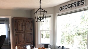 A dining area with a round table, black chairs, and a fruit bowl. A wooden cabinet and a 'GROCERIES' sign are visible. - Masters Rental Conveniently Located to Augusta National (Aiken)