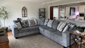 A living room with a grey sectional sofa, patterned throw pillows, a wooden coffee table, and a ceiling fan. - Masters Rental Conveniently Located to Augusta National (Aiken)