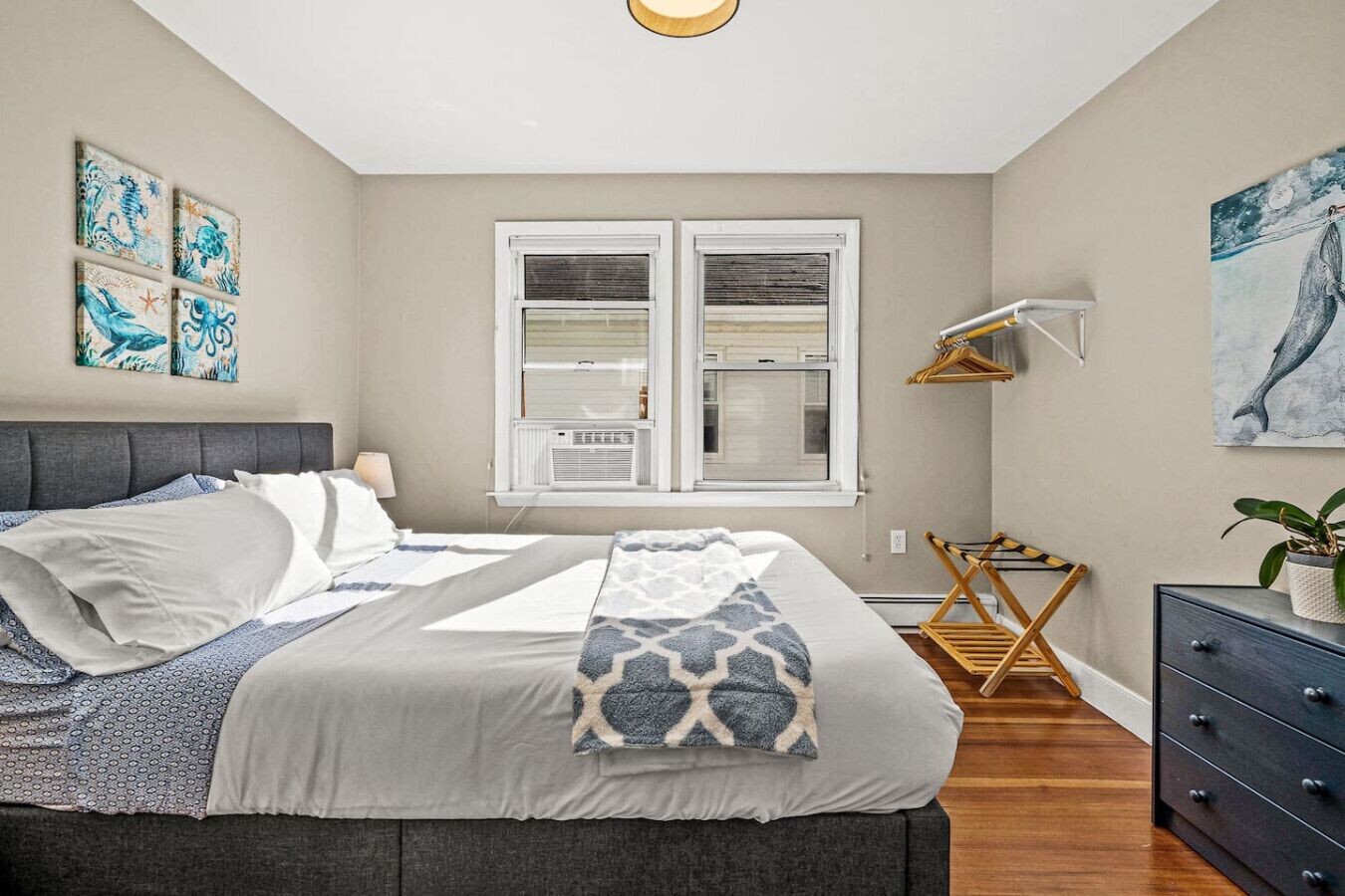 Une chambre à coucher avec un lit, une commode, une fenêtre et des œuvres d’art accrochées aux murs.