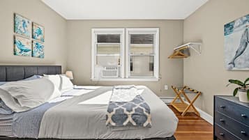 Une chambre à coucher avec un lit, une commode, une fenêtre et des œuvres d’art accrochées aux murs.