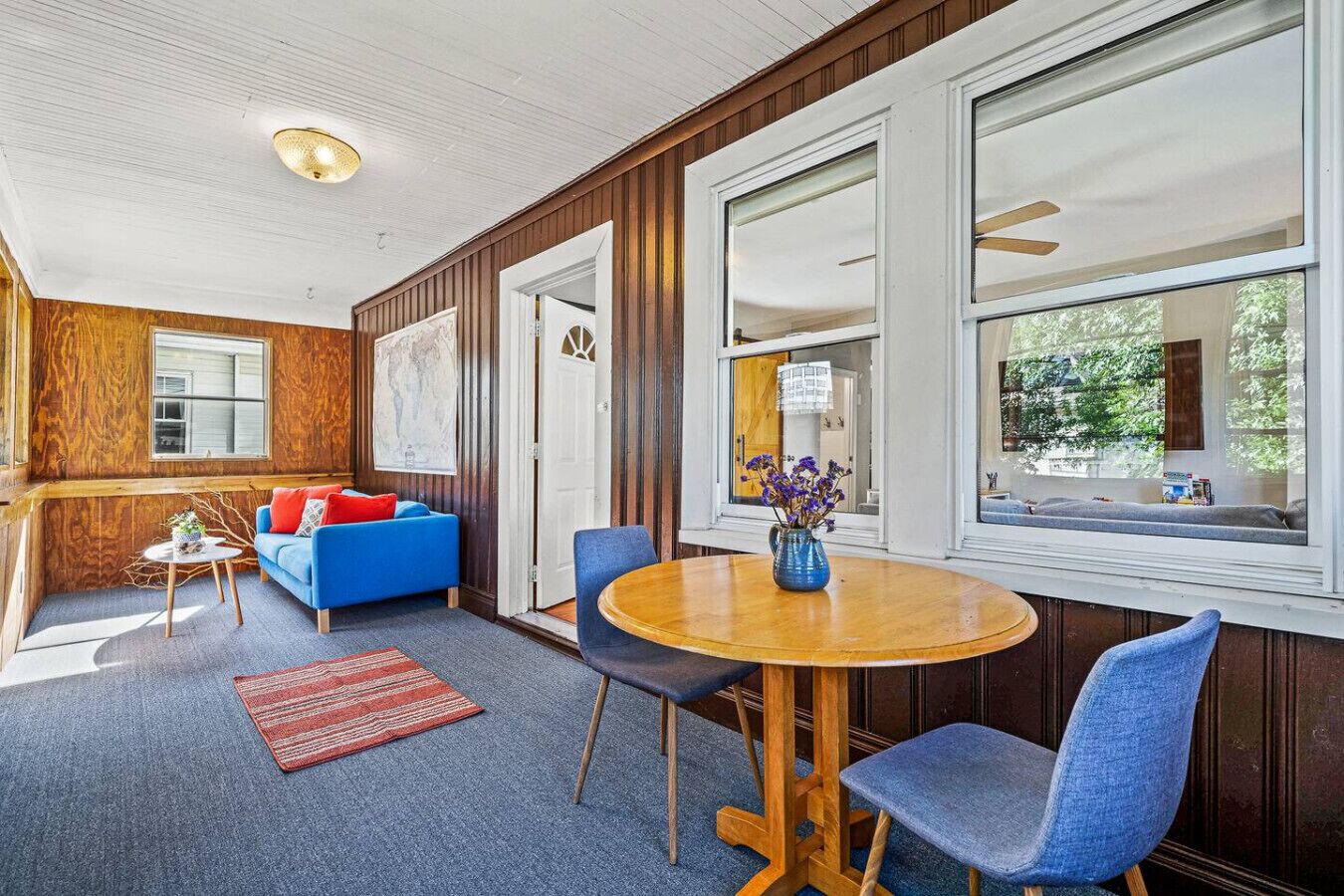 Una habitación acogedora con un sofá azul, una mesa de comedor de madera y una ventana con vistas al verdor.
