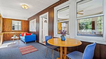 Una habitación acogedora con un sofá azul, una mesa de comedor de madera y una ventana con vistas al verdor.