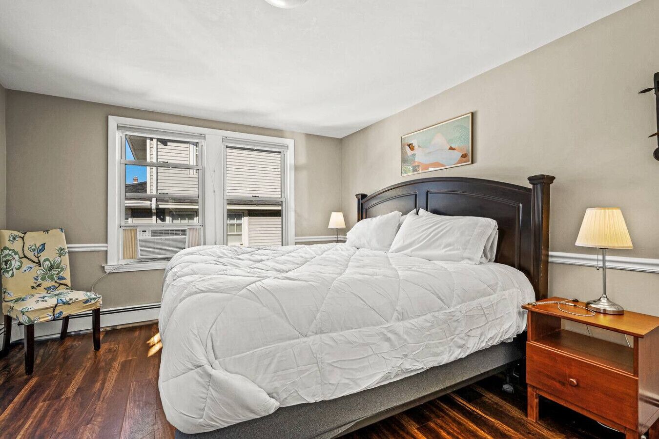 A bedroom with a large bed, a chair, a nightstand, and a window with blinds.