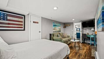 Un dormitorio con cama, escritorio, silla, una mesita, sofá y un cuadro de una escena de playa.