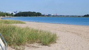 A sandy beach with a clear view of the water and a distant shoreline with buildings.
