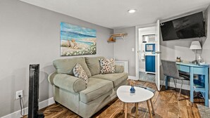 A living room with a sofa, a small table, a TV, and a desk with a chair.