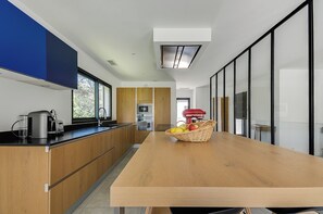 A modern kitchen with wooden cabinets, a black countertop, a large wooden table, and a fruit basket.