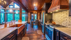 A modern kitchen with a large island, stainless steel appliances, and a brick backsplash. - Stunning copper tub room, outdoor Jacuzzi with view of Pine Lake (Broken Bow)