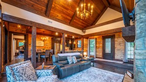 A spacious living room with a large sofa, a patterned armchair, and a dining area with a table and chairs. - Stunning copper tub room, outdoor Jacuzzi with view of Pine Lake (Broken Bow)