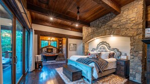 A bedroom with a stone wall, a large bed, a wooden ceiling, and a view of the outdoors. - Stunning copper tub room, outdoor Jacuzzi with view of Pine Lake (Broken Bow)