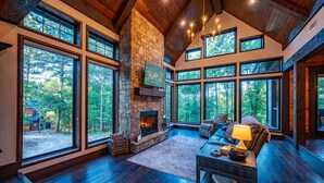 A spacious living room with a stone fireplace, large windows, and a cozy seating area. - Stunning copper tub room, outdoor Jacuzzi with view of Pine Lake (Broken Bow)