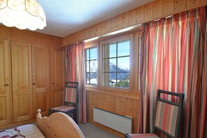 Ein Zimmer mit Holzwandverkleidung, einem Bett, zwei Sesseln, einem Heizkörper und einem fenster mit Vorhängen.