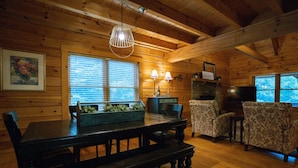 A wooden cabin interior with a dining table, chairs, a bench, a television, and a fireplace.