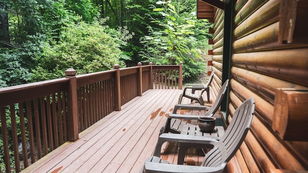 A wooden deck with a railing, surrounded by dense greenery.