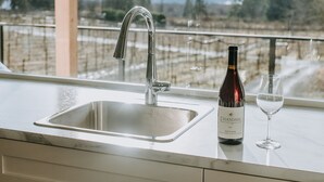 Une cuisine avec un évier en acier inoxydable, une bouteille de vin et un verre posés sur le comptoir.
