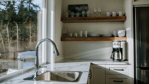 Une cuisine équipée d’un évier, d’une machine à café et d’étagères en bois au-dessus du plan de travail.