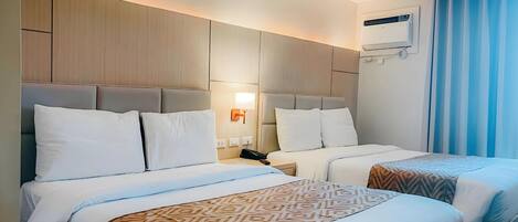 A hotel room with two beds, a ceiling fan, an air conditioning unit, and a window with curtains.