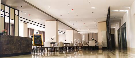 A spacious, modern hotel lobby with a reception desk, seating area, and a large mirror.
