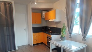 Eine kleine Küche mit orangefarbenen Schränken, einer weißen Arbeitsplatte und einem Topf mit Pflanze auf einem kleinen Tisch.