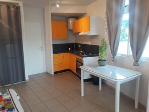 A compact kitchen with orange cabinets, a white countertop, and a potted plant on a small table. - A sweet and confortable studio downtown Papeete (Papeete)