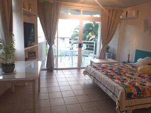A hotel room with a bed, a desk, a chair, and a balcony with a table and chairs. - A sweet and confortable studio downtown Papeete (Papeete)