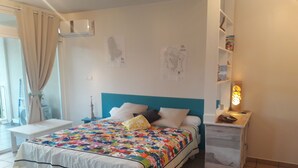 Ein Schlafzimmer mit Bett, Nachttisch, Wandklimaanlage und einem Fenster mit Vorhängen.