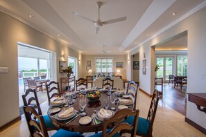 A dining room with a round table set for six, surrounded by wooden chairs with blue cushions.