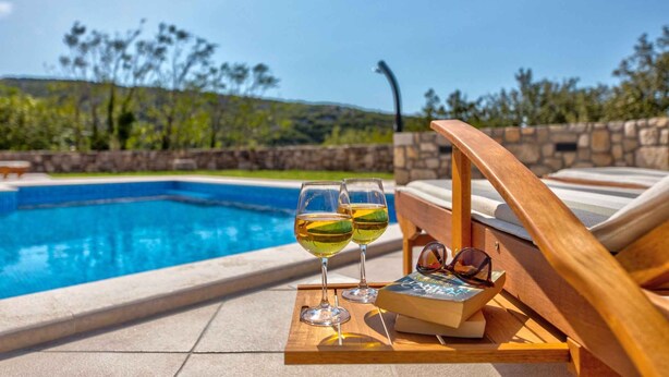 A poolside setting with two glasses of white wine, a book, and sunglasses on a wooden tray. - Holiday home mit Pool und Klimaanlage (Barci)