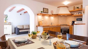 A modern kitchen with wooden cabinets, a microwave, and a dining area with a table set for two. - Holiday home mit Pool und Klimaanlage (Barci)