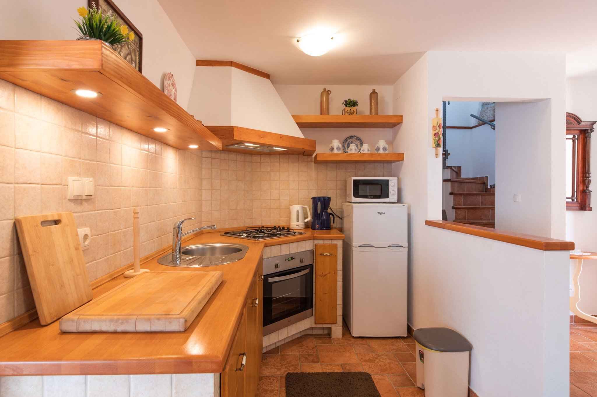 Une cuisine compacte dotée de plans de travail en bois, d’un four encastré, d’un four à micro-ondes et d’un évier.