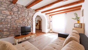 A living room with stone walls, wooden beams, a television, a sofa, and a plant. - Holiday home mit Pool und Klimaanlage (Barci)