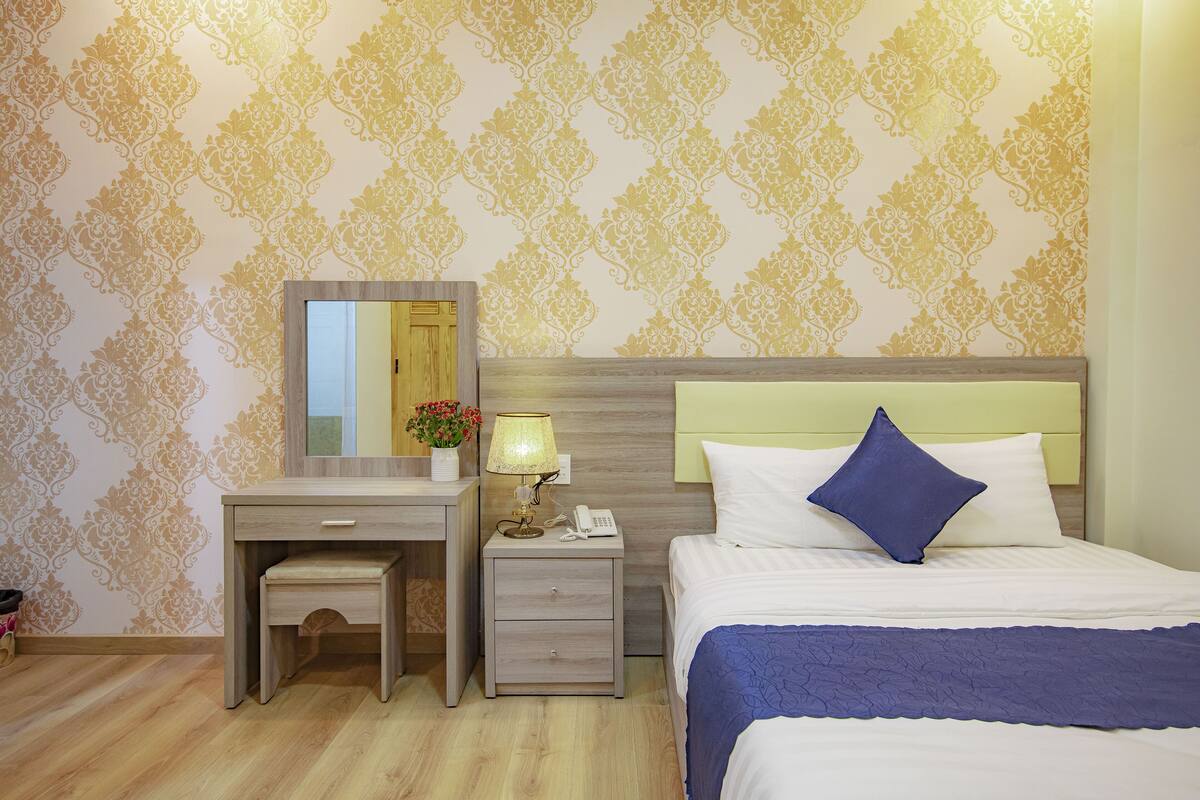 Quarto de hotel com uma cama, uma escrivaninha com luminária, mesa de cabeceira e um espelho.