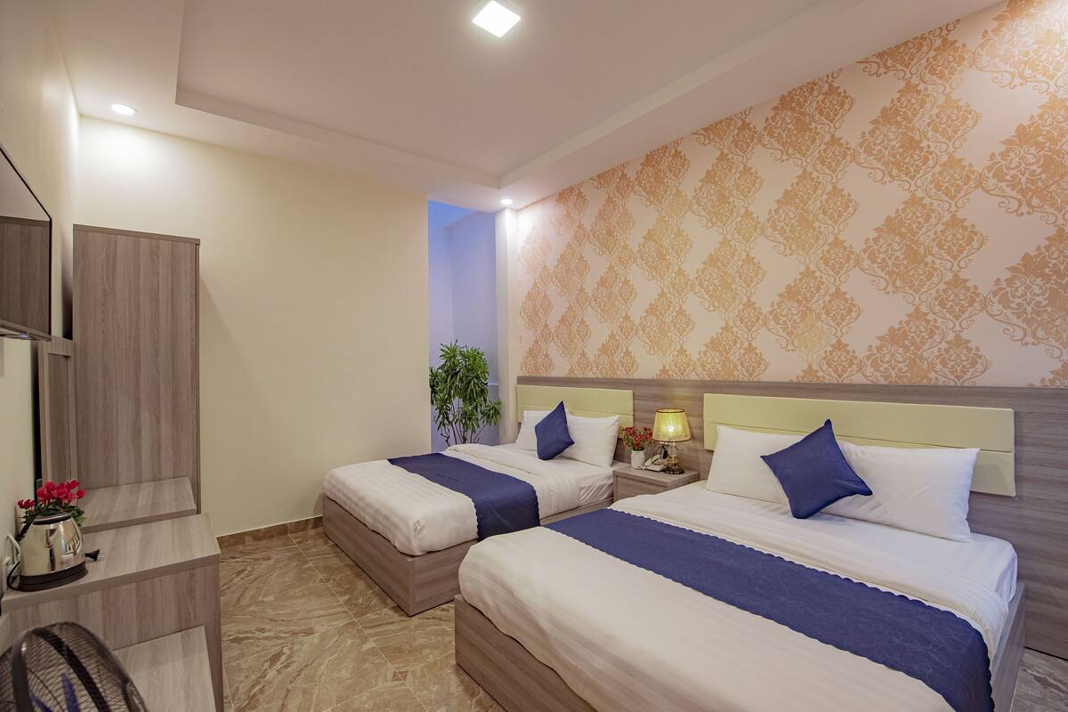 Quarto de hotel com duas camas, uma escrivaninha e um espelho.