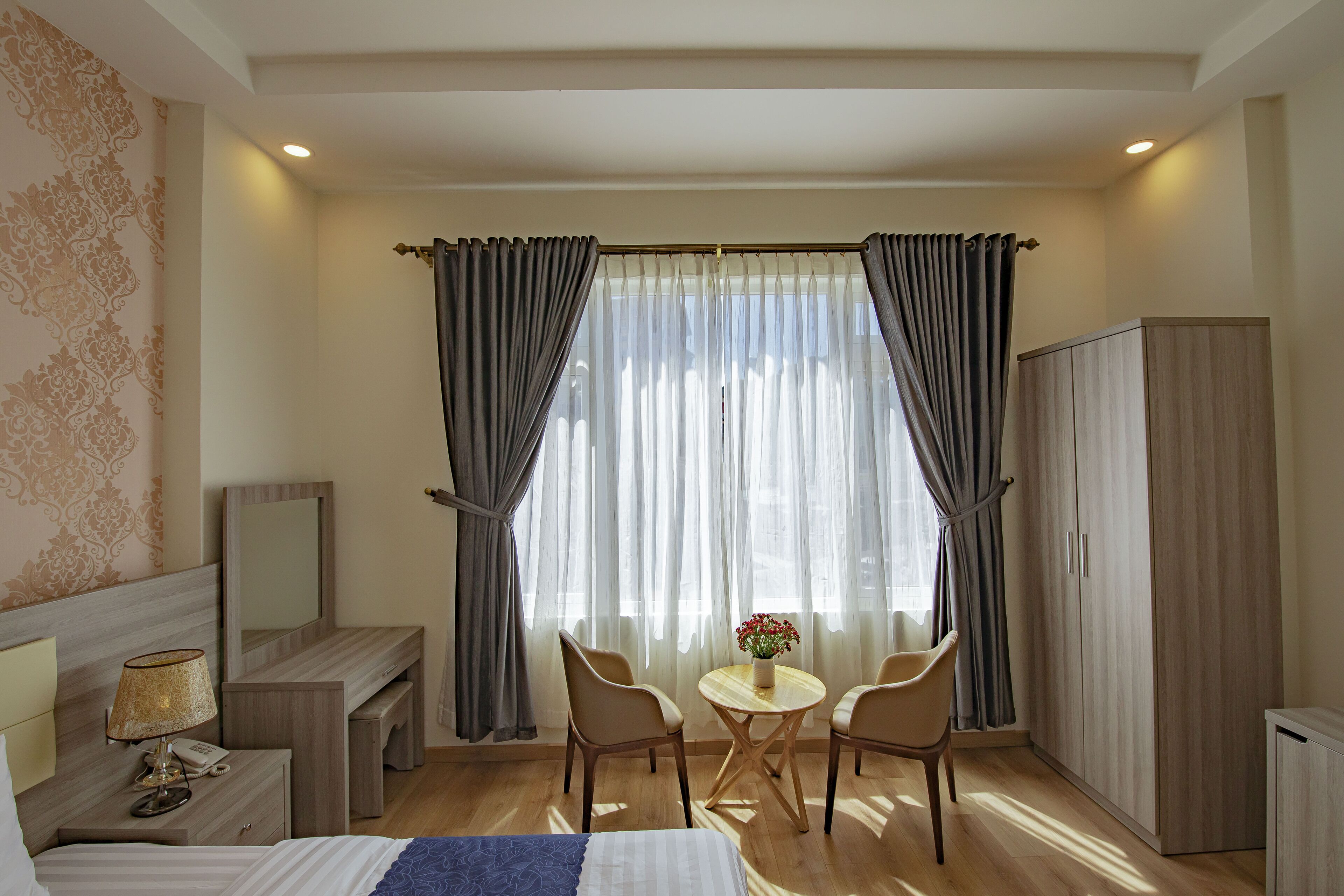 Ein Hotelzimmer mit Bett, Nachttisch, Lampe, Spiegel, Schreibtisch, Stuhl, Tisch mit Blumen und einem Kleiderschrank.