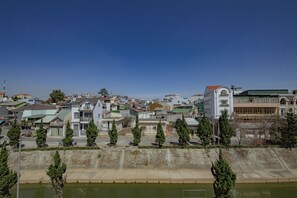 A residential area with houses, a large white building with a red roof, and a river in the foreground. - Khanh Uyen Hotel (Xuan Huong - Da Lat)