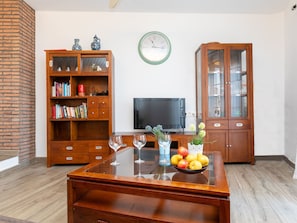 Una sala de estar con una mesa de centro de madera, una estantería, un televisor y un reloj en la pared.