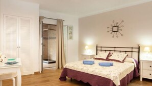 Un dormitorio con cama, mesitas de noche, un escritorio, cabina de ducha de vidrio y un reloj de pared.