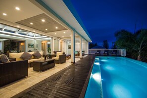 An indoor swimming pool area with a covered patio, lounge chairs, and a poolside table. - Luxury 4BR Villa in Silver Sands Beach Resort, Trelawny, Jamaica (Duncans)