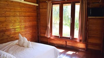 A wooden cabin room with a bed, a window with curtains, and a television on the wall.