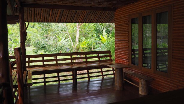 A wooden bench and table on a porch with a view of lush greenery. - Pru Valley Thaley Tai Resort (Chumphon)