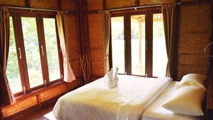 A large bed with white linens and pillows, wooden walls, and large windows with curtains. - Pru Valley Thaley Tai Resort (Chumphon)