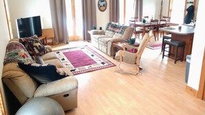Amplia sala de estar con sofá, sillones, una mesa de centro y un comedor con mesa y sillas.