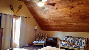 Una habitación acogedora con techo inclinado, una cama, un sofá estampado, una silla y una mesita.